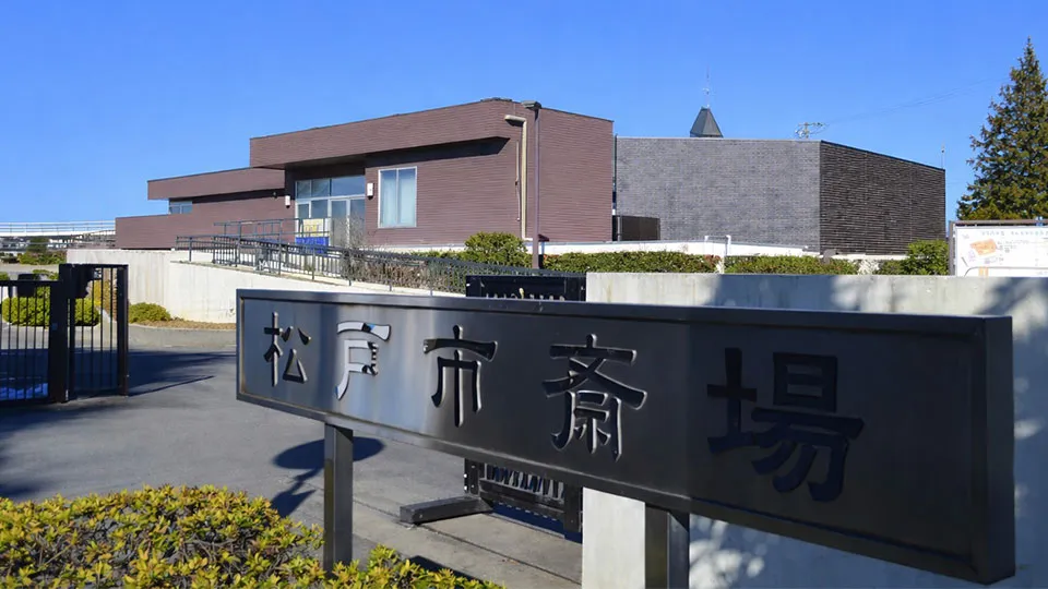 松戸市斎場の入口の銘板と、茶色い外壁の斎場の建物